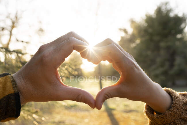 Руки чоловіка і жінки роблять символ у формі серця під час заходу сонця. — стокове фото