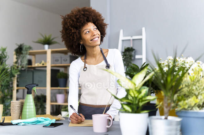 Florista reflexiva mirando hacia otro lado mientras está de pie junto a la mesa en la tienda - foto de stock