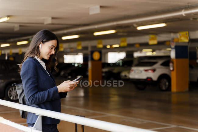 Жіночий професіонал, стоячи на парковці, користується смартфоном. — стокове фото