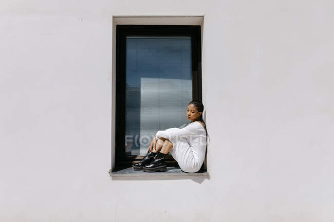 Jeune femme assise sur le rebord de la fenêtre — Photo de stock