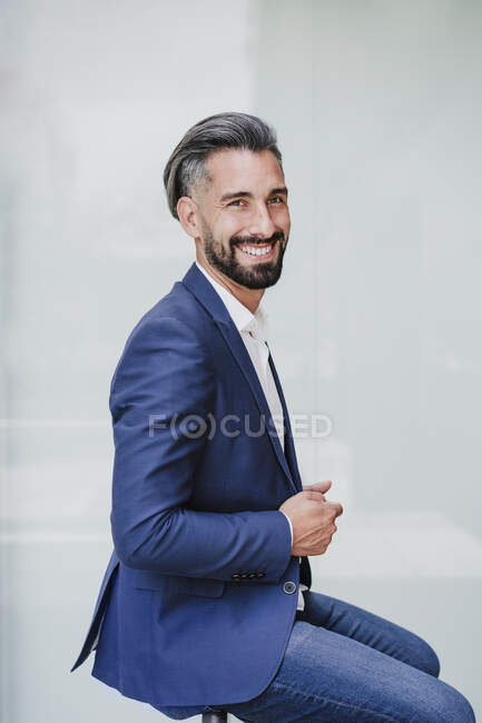 Бизнесмен улыбается, сидя у белой стены — стоковое фото