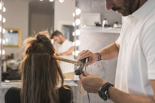 Чоловічий перукар, використовуючи випрямлення на волоссі жіночого клієнта в салоні — стокове фото
