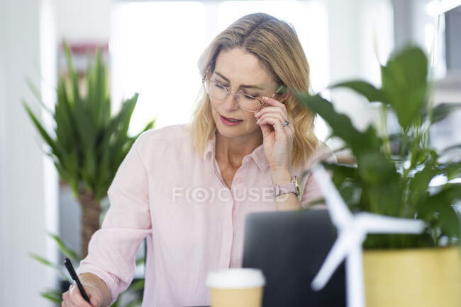 Зрелая деловая женщина, держащая очки во время работы в домашнем офисе — стоковое фото