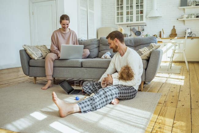 Femme d'affaires souriante et homme d'affaires avec sa fille travaillant sur un ordinateur portable à la maison — Photo de stock
