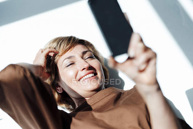 Mujer de negocios sonriente usando el teléfono inteligente mientras está acostado en el suelo en la oficina - foto de stock
