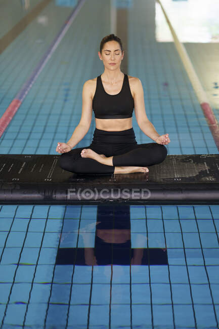 Mid adult woman in lotus position sitting on raft floating in swimming pool — Stock Photo