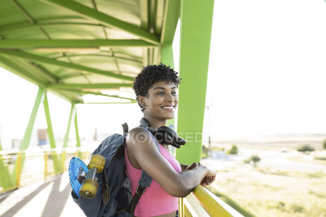 Молода жінка з рюкзаком і навушниками стоїть на мосту. — стокове фото
