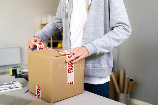 Male entrepreneur sticking tape on cardboard box at warehouse — Stock Photo