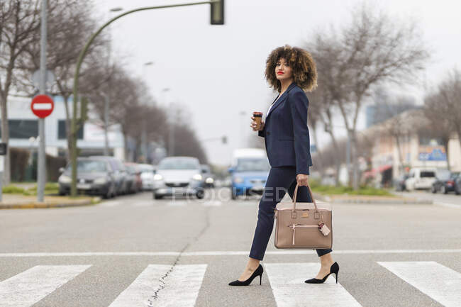 Well-dressed businesswoman with purse crossing road in city — Stock Photo