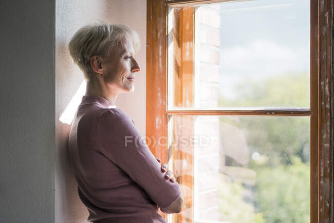 Femme d'affaires souriante regardant par la fenêtre tout en s'appuyant sur le mur — Photo de stock
