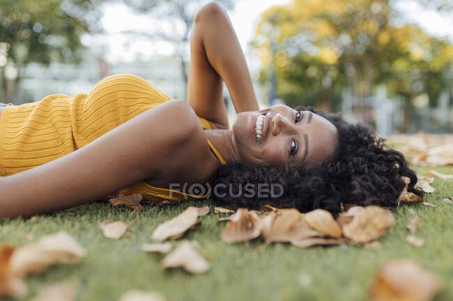 Sorrindo bela mulher de cabelos encaracolados deitada na grama no parque no outono — Fotografia de Stock