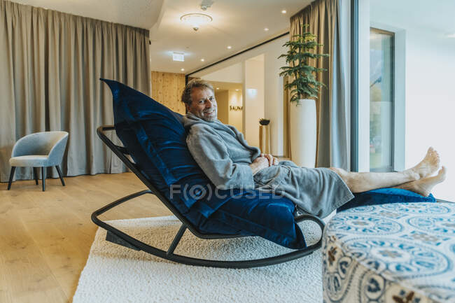 Homem de roupão relaxante na cadeira de balanço no quarto de hotel — Fotografia de Stock