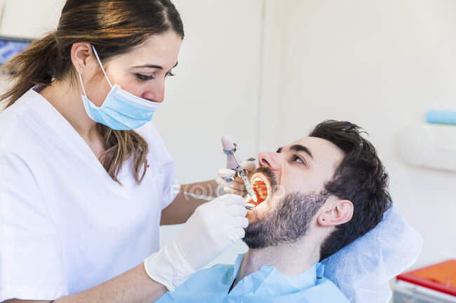 Female dentist wearing protective face mask examining male patient's teeth at medical clinic — Stock Photo