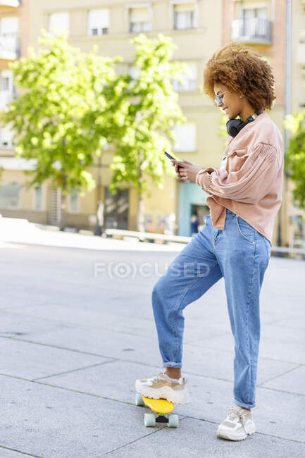 Молодая женщина с помощью смартфона, стоя на скейтборде на тропинке — стоковое фото