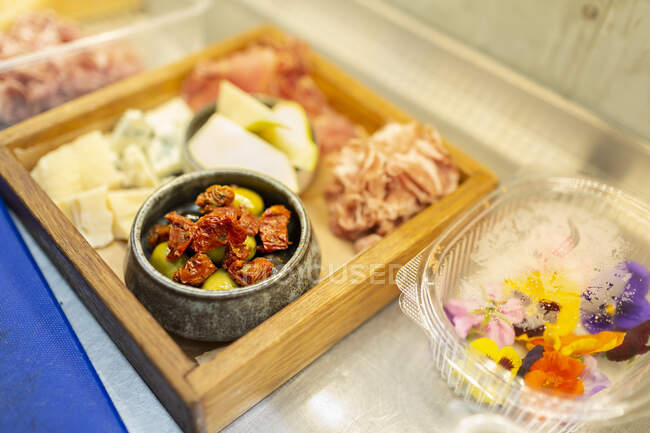Dried chili pepper served with olives in wooden tray by edible flowers in container — Stock Photo