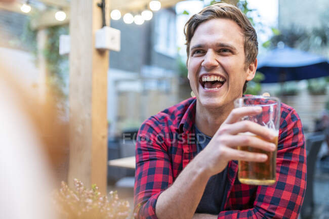 Hombre riendo mientras sostiene vaso de cerveza en el pub - foto de stock