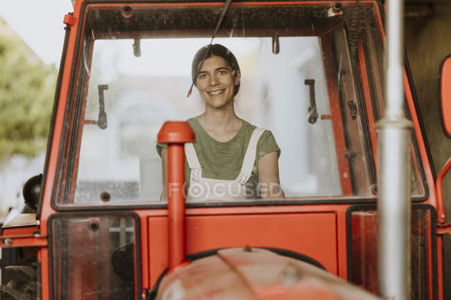 Улыбающаяся работница фермы сидит в тракторе и видит это через лобовое стекло. — стоковое фото