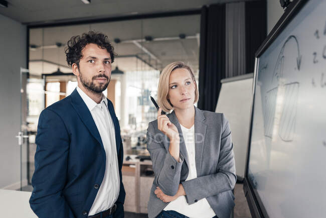Mid adult partners standing by projection screen in office — Stock Photo