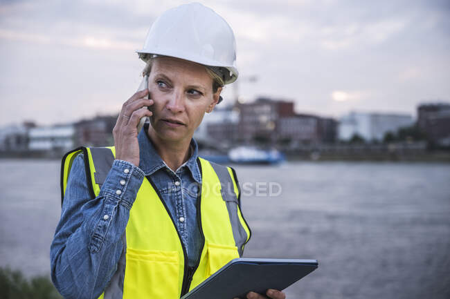Profesional femenino mirando hacia otro lado hablando en el teléfono inteligente mientras sostiene la tableta digital - foto de stock