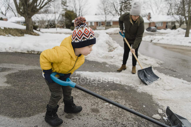 Сын помогает матери, убирая снег на дороге. — стоковое фото