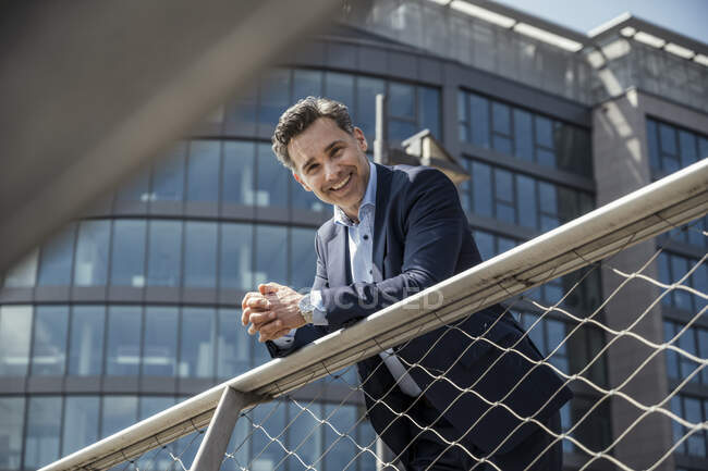Reifer Geschäftsmann lächelt, während er sich an einem sonnigen Tag an Geländer lehnt — Stockfoto