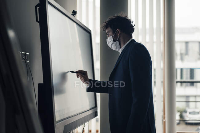 Homme entrepreneur avec masque visage écriture sur écran de projection dans le bureau — Photo de stock