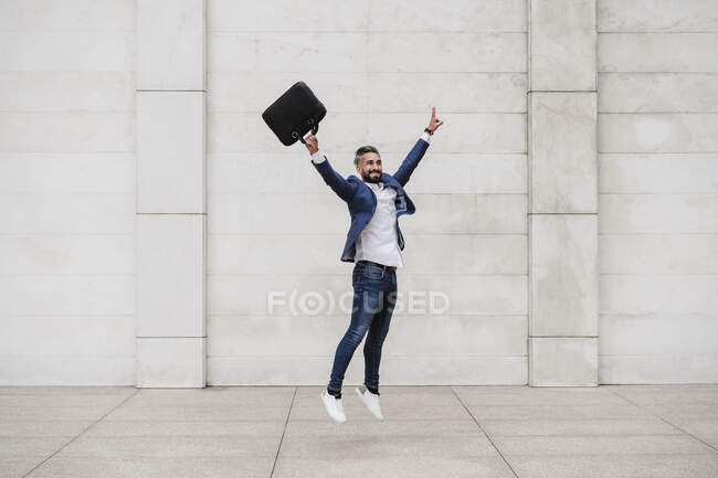 Carefree businessman with hand raised jumping on footpath — Stock Photo
