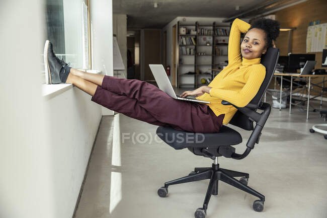 Professionista femminile con computer portatile seduto sulla sedia in ufficio — Foto stock