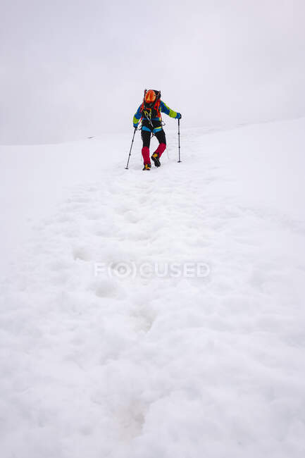 Male hiker climbing snowcapped mountain with hiking poles — Stock Photo