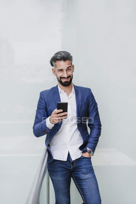 Confident businessman with mobile phone standing by railing — Stock Photo