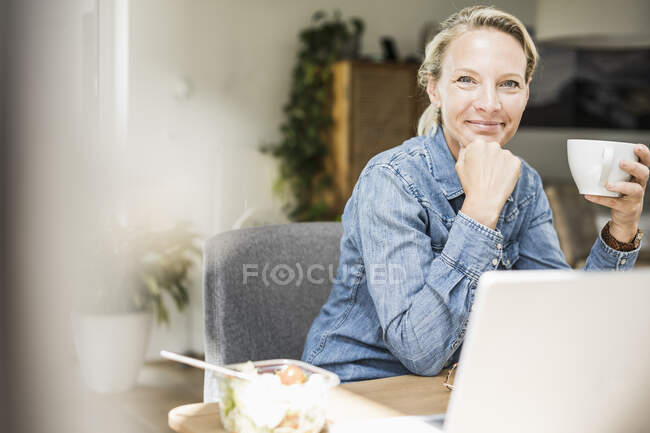 Mujer de negocios sonriente con taza de café en la oficina en casa - foto de stock