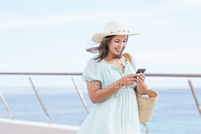 Улыбающаяся взрослая женщина в шляпе с помощью смартфона — стоковое фото