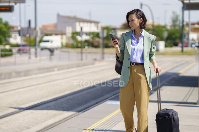 Female professional using smart phone while waiting for train at railroad station — Stock Photo