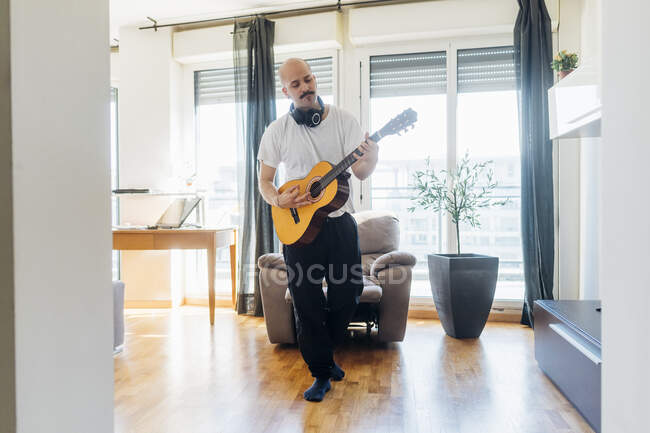 Jeune guitariste masculin jouant devant une chaise inclinable à la maison — Photo de stock