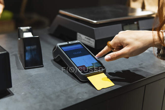 Cliente femenino ingresando contraseña al lector mientras paga con tarjeta de crédito en tienda minorista - foto de stock