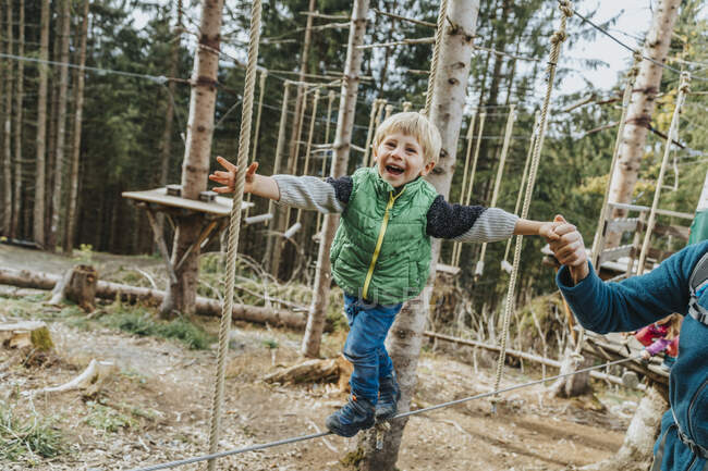 Ragazzo giocoso che fa corso di corda mentre sostenuto dal padre nella foresta a Salzburger Land, Austria — Foto stock