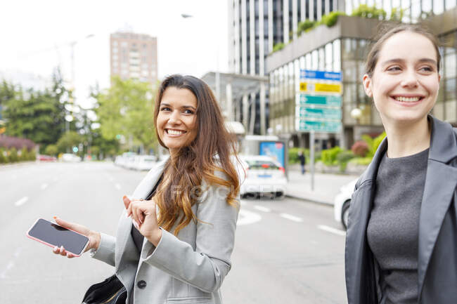 Donna d'affari con cellulare che cammina su strada con un collega in città — Foto stock