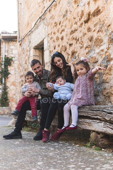 Счастливая семья сидит на скамейке с домом на заднем плане — стоковое фото