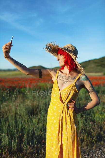 Улыбающаяся женщина с рукой на бедре делает селфи через смартфон на поле — стоковое фото