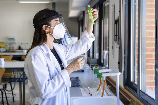 Jovem cientista usando máscara protetora examinando química em laboratório — Fotografia de Stock