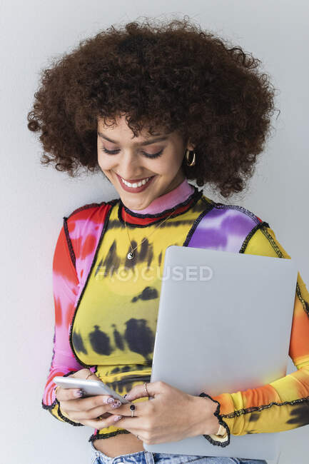 Donna sorridente con computer portatile utilizzando il telefono cellulare su sfondo bianco — Foto stock