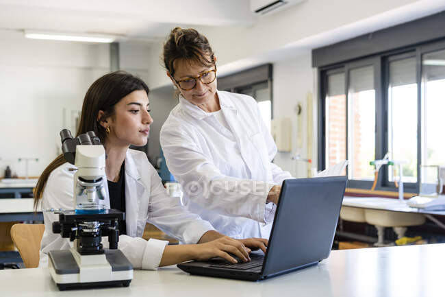 Femme scientifique mature et jeune collègue discutant sur ordinateur portable au laboratoire — Photo de stock