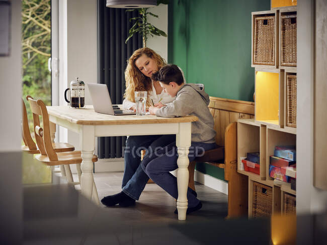 Mère enseignant son fils à la maison devant un ordinateur portable à la maison — Photo de stock