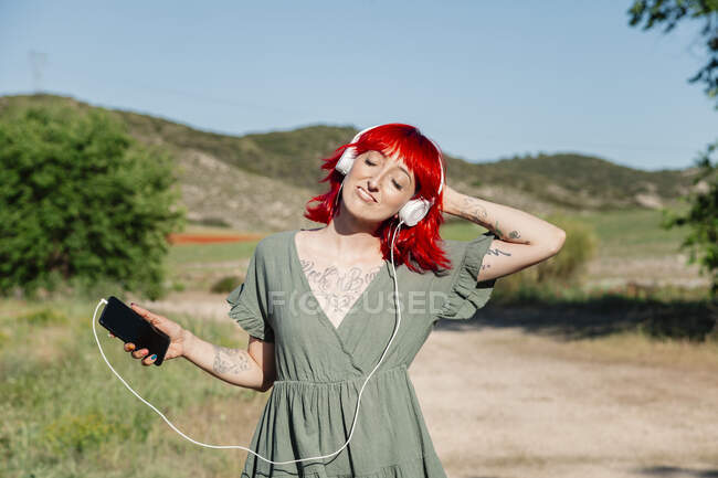 Young woman with hand in hair listening music on field during sunny day — Stock Photo