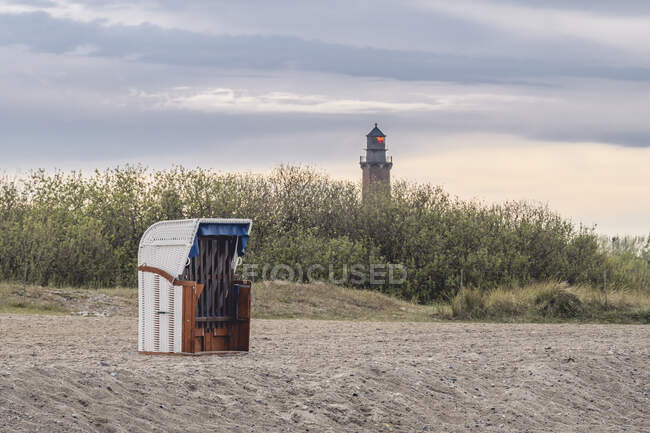 Chaise de plage à capuche debout sur la plage vide au crépuscule avec phare de Neuland en arrière-plan — Photo de stock