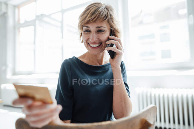 Donna d'affari sorridente con carta di credito che parla al cellulare in ufficio — Foto stock