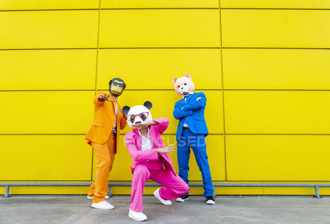 Three adults wearing vibrant suits and animal masks posing together in front of yellow wall — Stock Photo