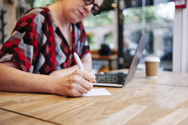 Жінка пише на папері за столом у кафе. — стокове фото