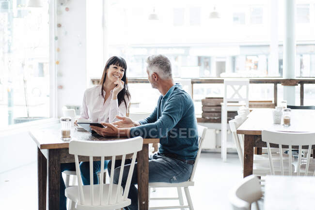 Empresario con tableta digital explicando a su colega mientras está sentado en la cafetería - foto de stock