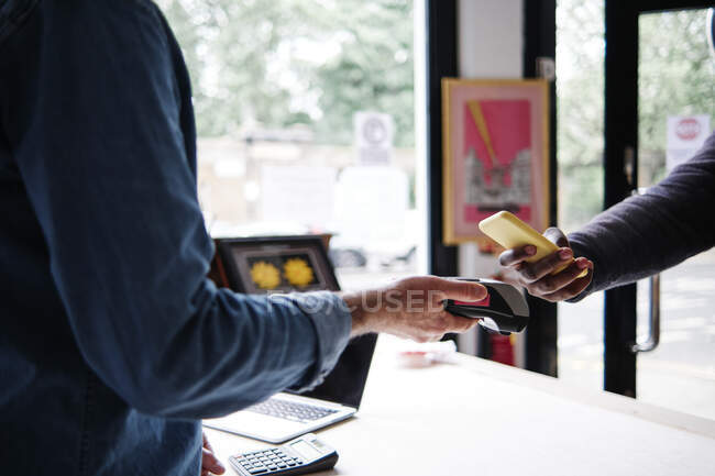Male customer using smart phone while making contactless payment in store — Stock Photo